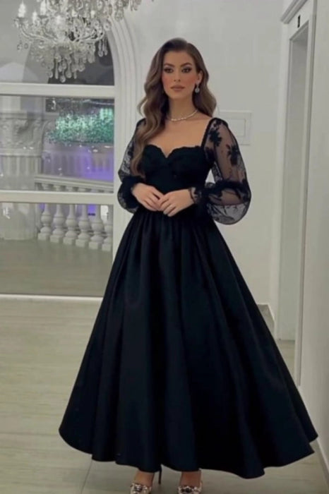 Woman wearing a black evening gown with sheer sleeves in an elegant indoor setting.